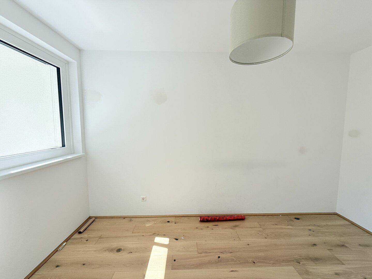 Helles Schlafzimmer mit Parkettboden und einem Fenster, das viel Tageslicht hereinlässt.
