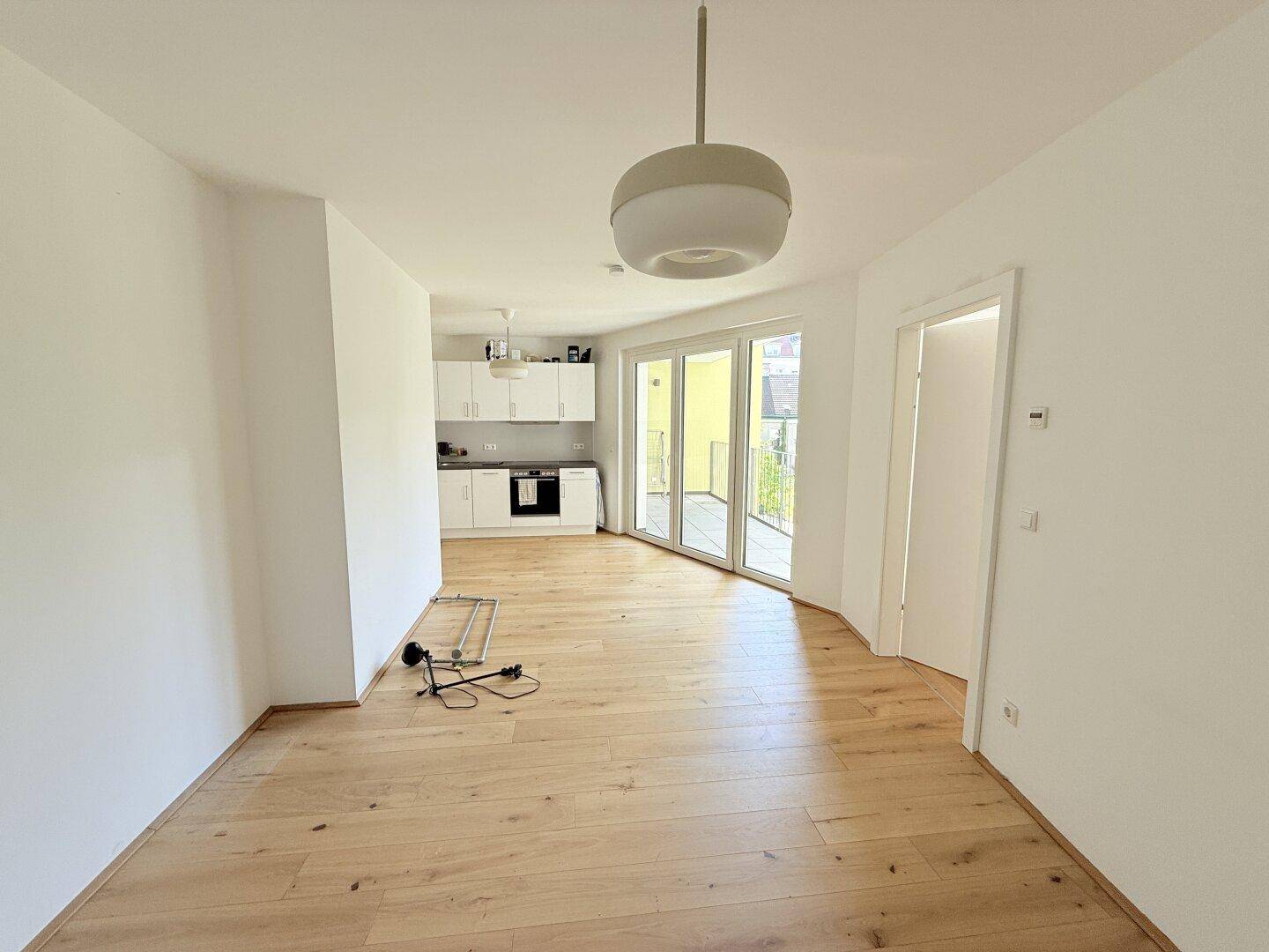 Geräumiger offener Wohnbereich mit Holzboden und Blick auf die moderne Einbauküche.