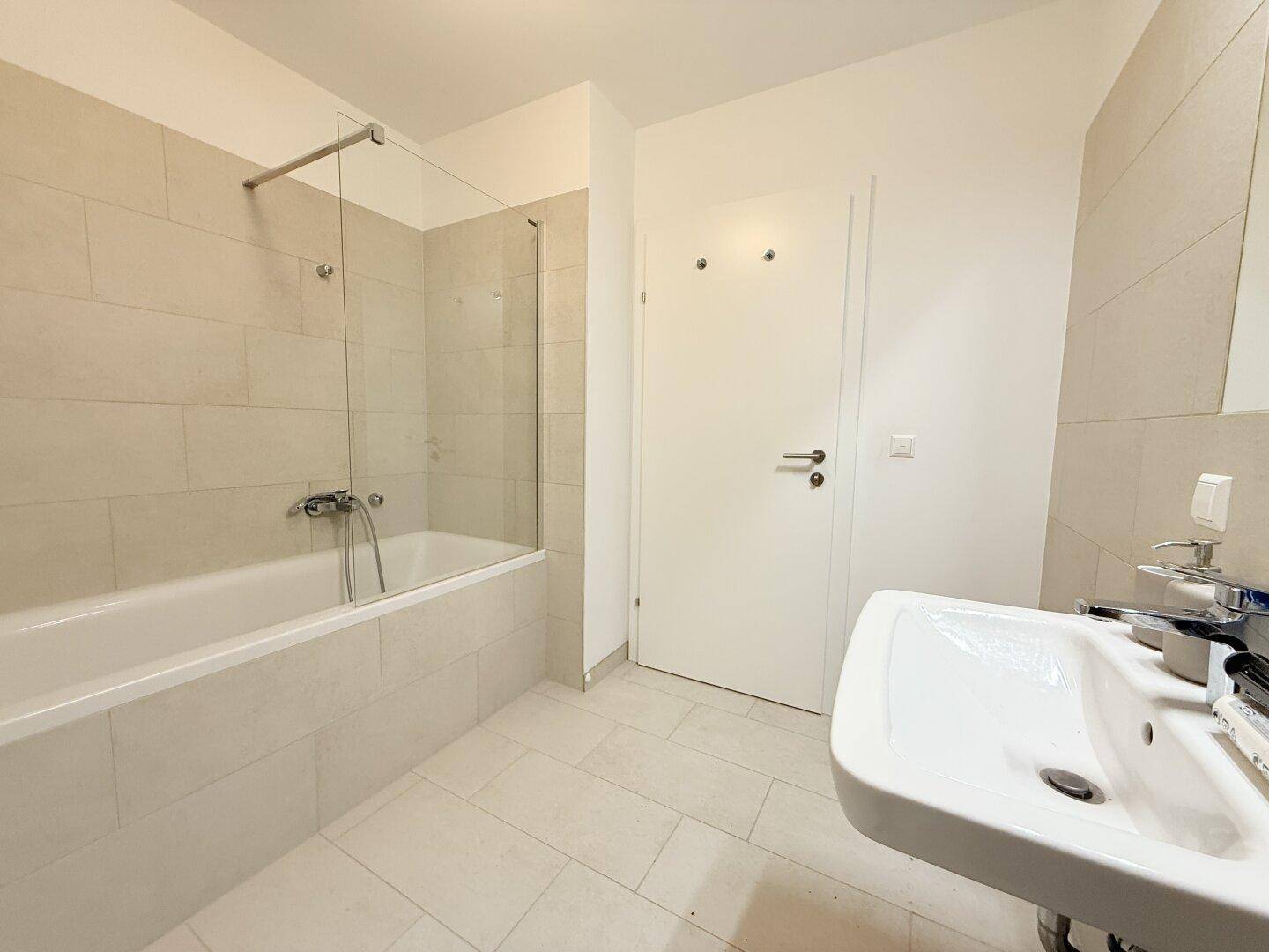Modernes Badezimmer mit Badewanne, Duschwand und Waschbecken mit Spiegel.
