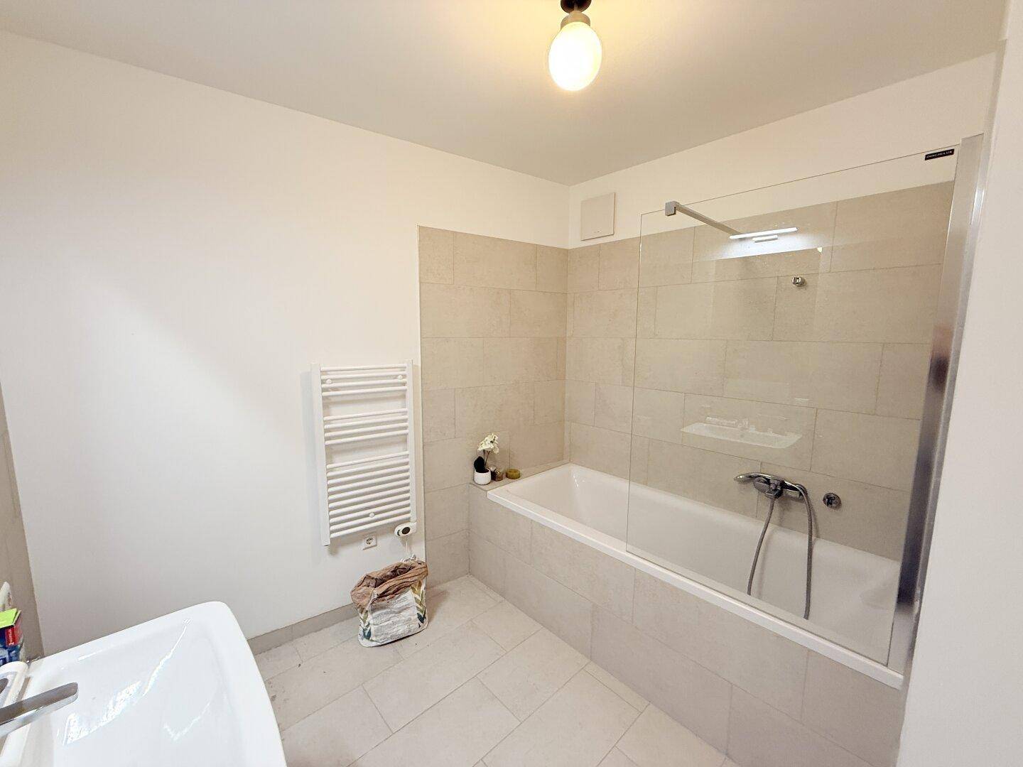 Helles Badezimmer mit Badewanne, Duschwand aus Glas und beigefarbenen Wandfliesen.