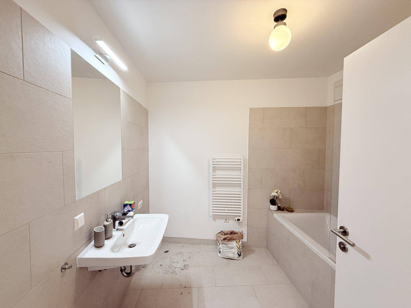 Modernes Badezimmer mit beigefarbenen Fliesen, Badewanne und einem beheizten Handtuchhalter.