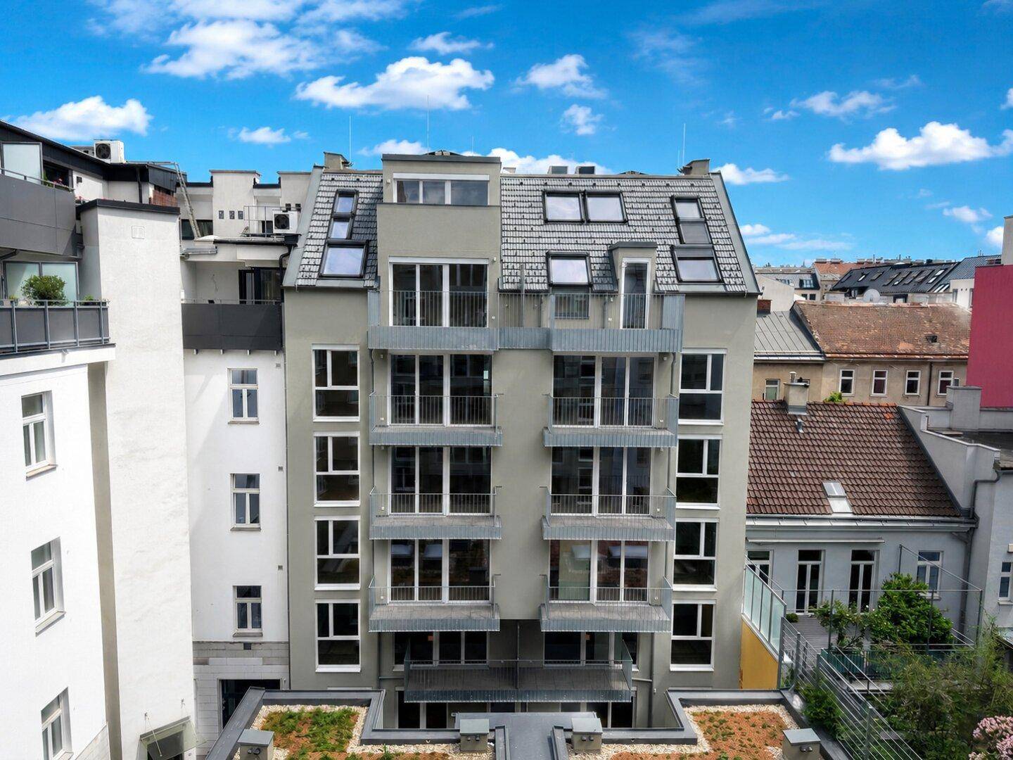 Moderne Gebäudefassade mit vielen Fenstern und Balkonen, umgeben von städtischer Architektur.