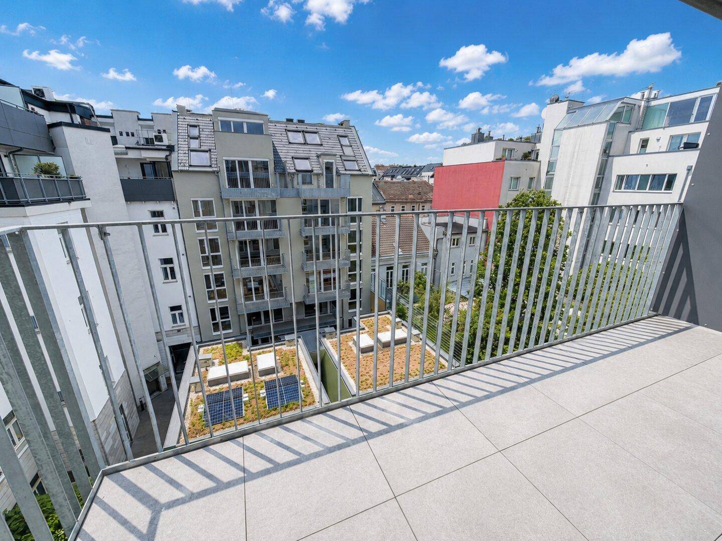 Geräumiger Balkon mit Fliesenboden und Metallgeländer, bietet Blick auf umliegende Gebäude und Gründächer.