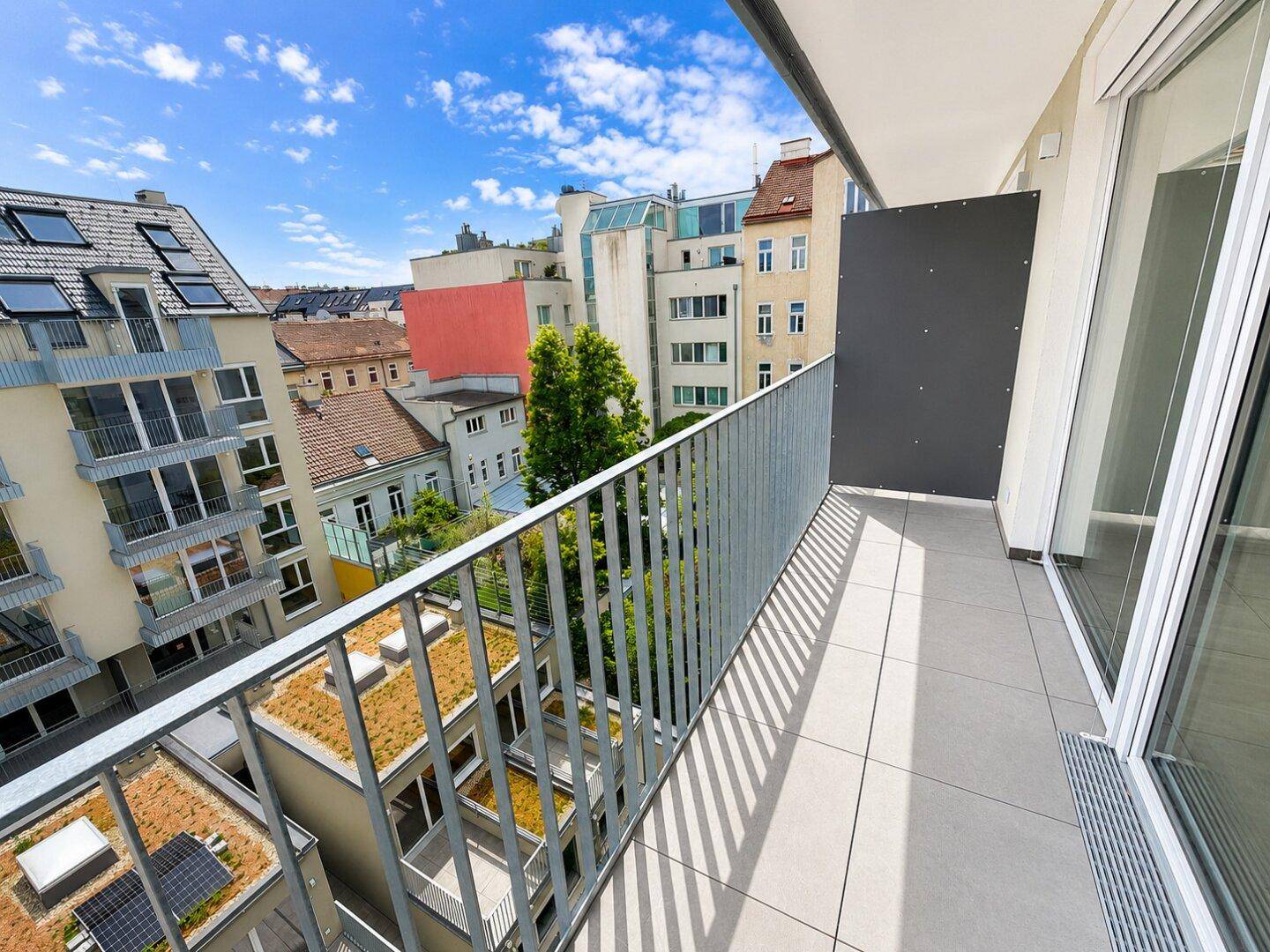 Sonniger Balkon mit Fliesenboden und Metallgeländer, bietet einen Ausblick auf die umliegenden Gebäude.