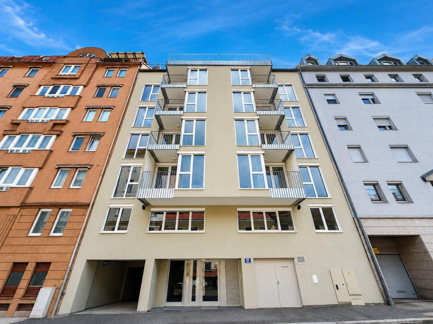 Moderne Wohnhausfassade mit zahlreichen Balkonen und großen Fenstern in urbaner Umgebung.