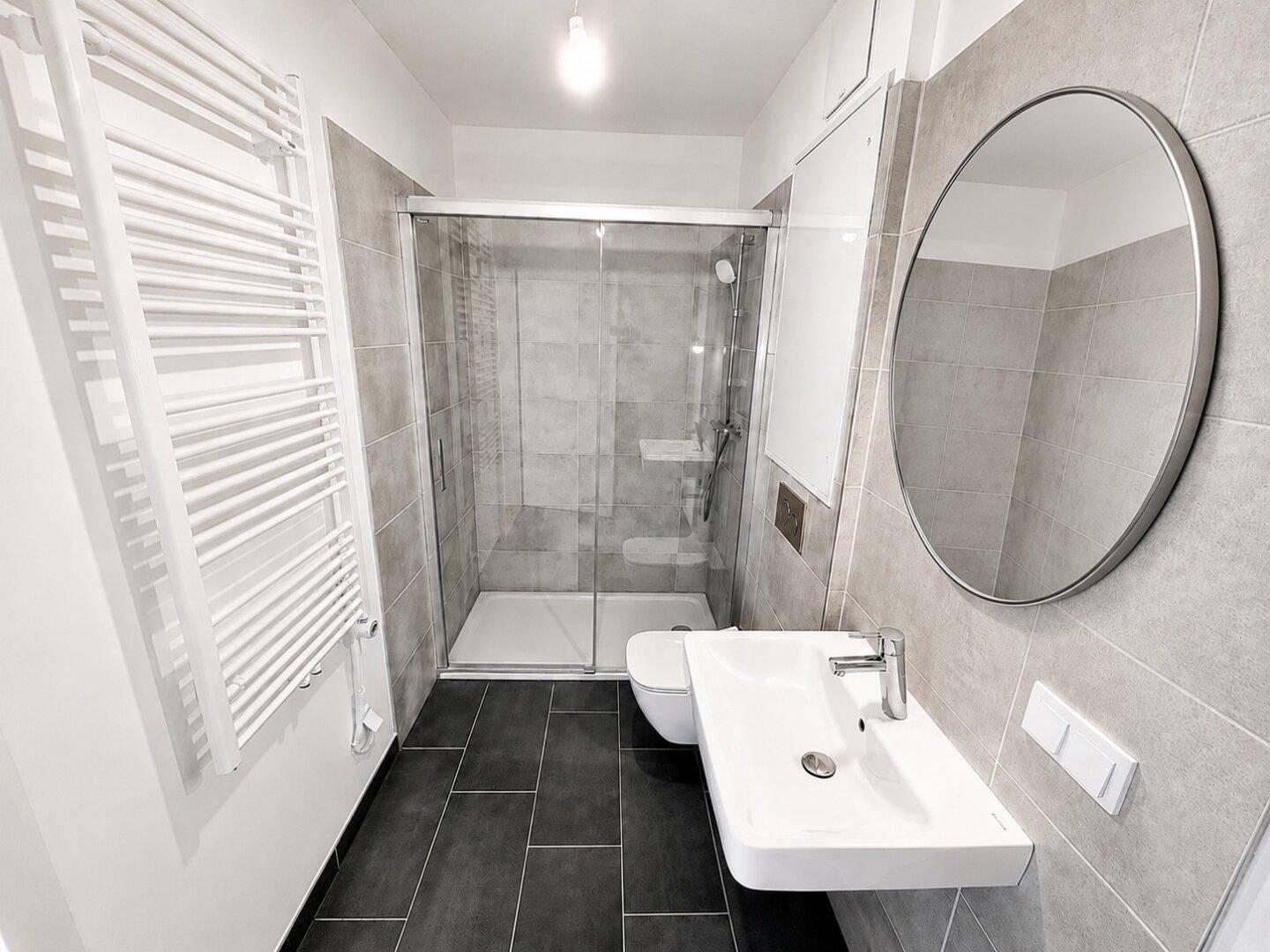 Modernes Badezimmer mit Duschkabine, Waschbecken, WC und beheiztem Handtuchhalter.