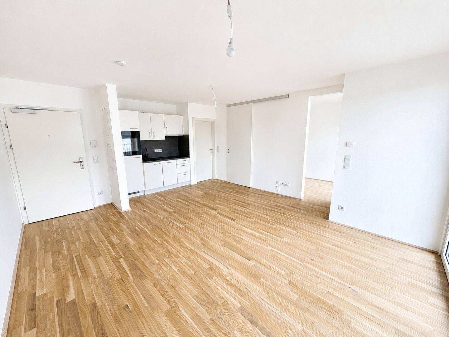 Offener Wohnbereich mit Holzboden und integrierter Küchenzeile in modernem Design.