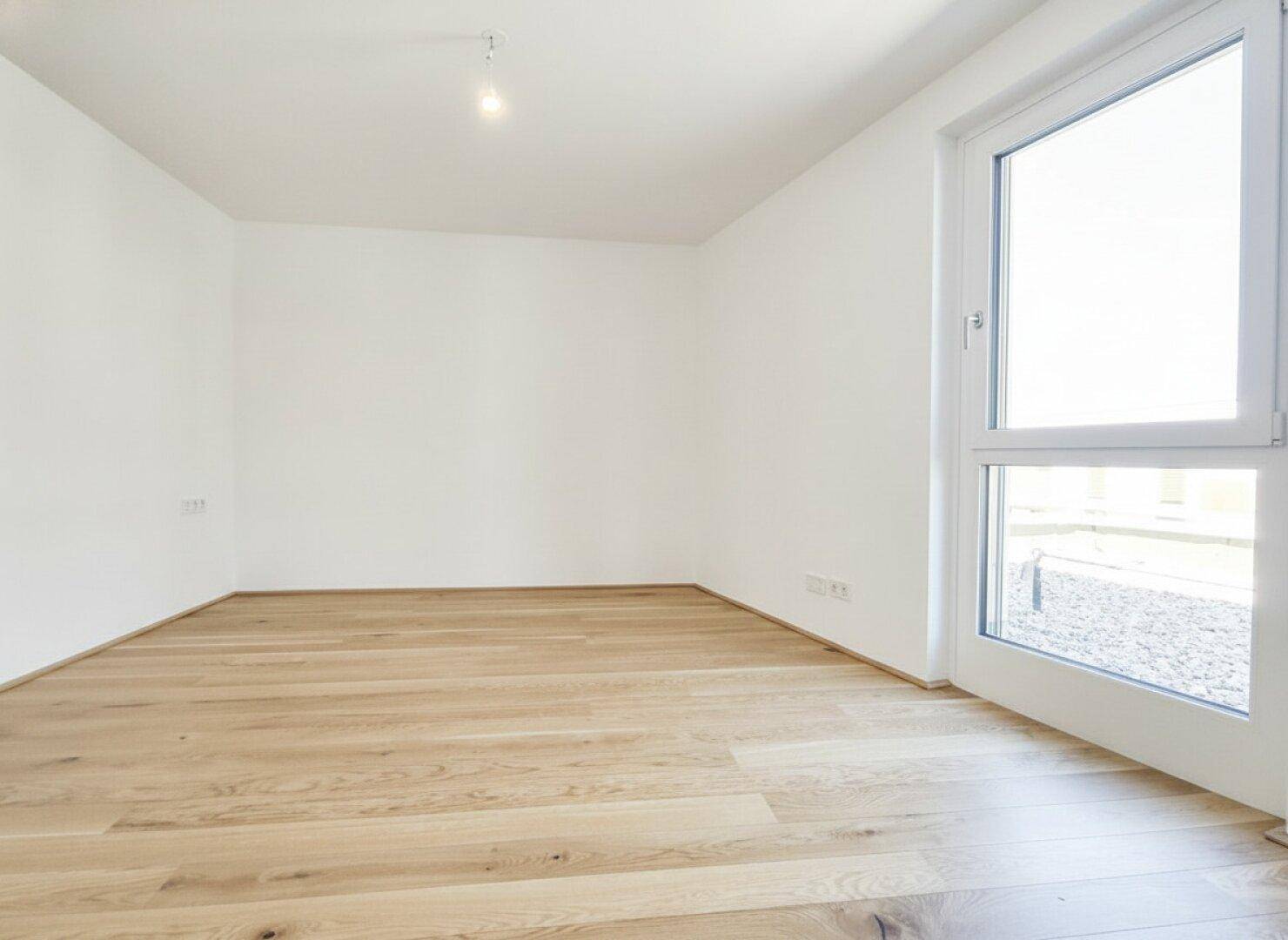 Ruhiges, helles Zimmer mit Holzdielenboden und Fenster zum Außenbereich, ideal als Schlafzimmer.