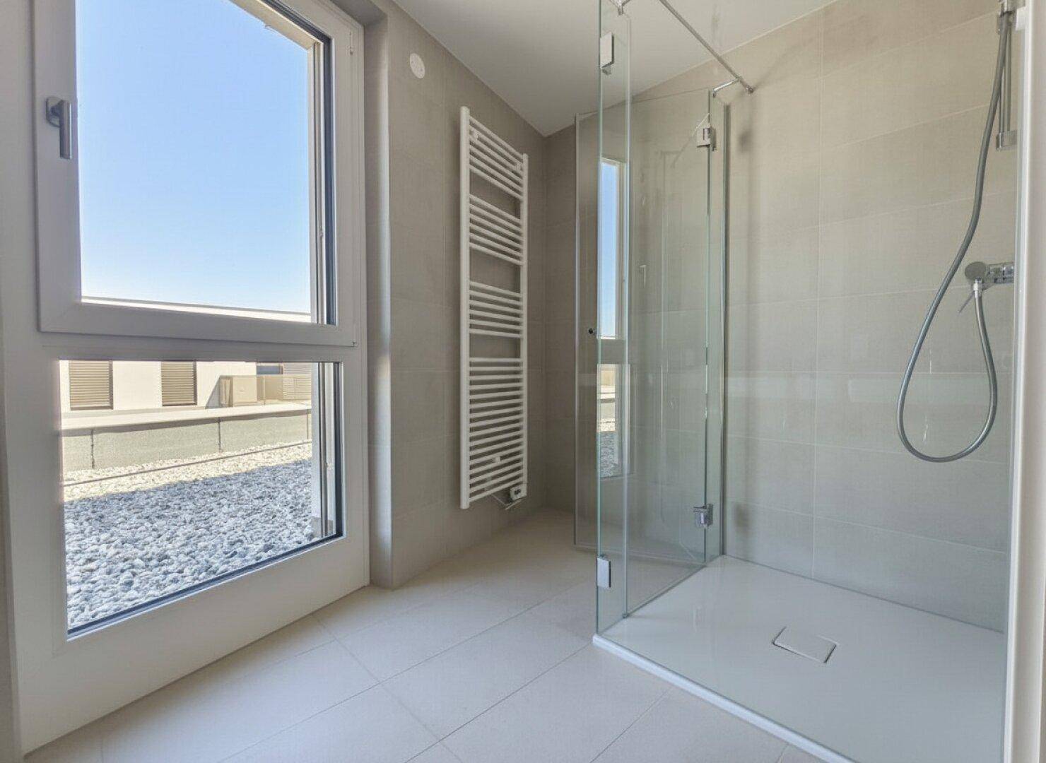 Modernes Badezimmer mit begehbarer Dusche, hellen Fliesen und beheiztem Handtuchhalter.