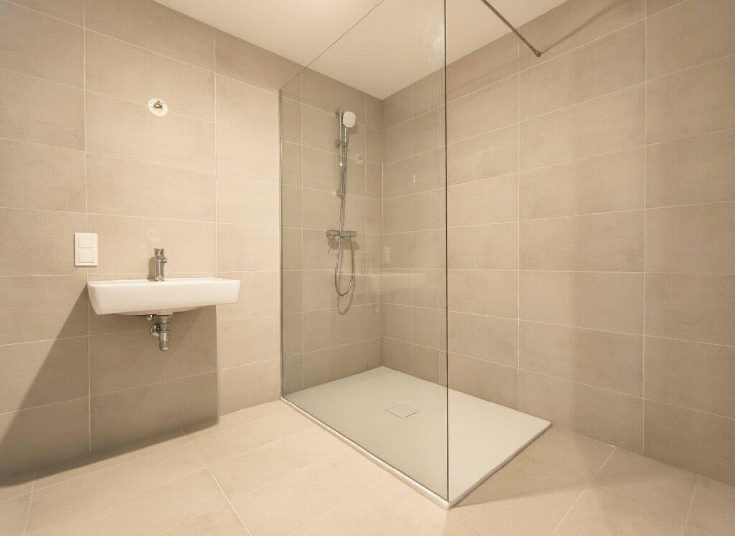 Modernes Badezimmer mit beigefarbenen Fliesen, wandhängendem Waschbecken und begehbarer Dusche.