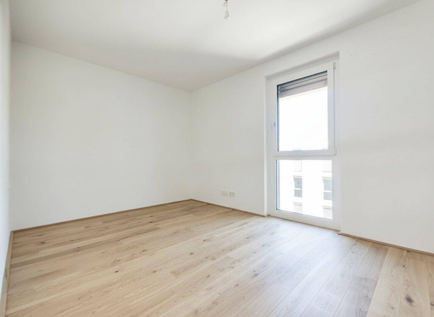 Ruhiges Schlafzimmer mit hellem Holzboden und einem Fenster, das viel Tageslicht hereinlässt.