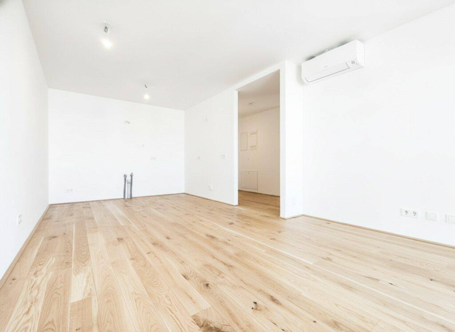 Heller Raum mit Holzboden und Anschlüssen für eine Küche, bereit für die Installation.
