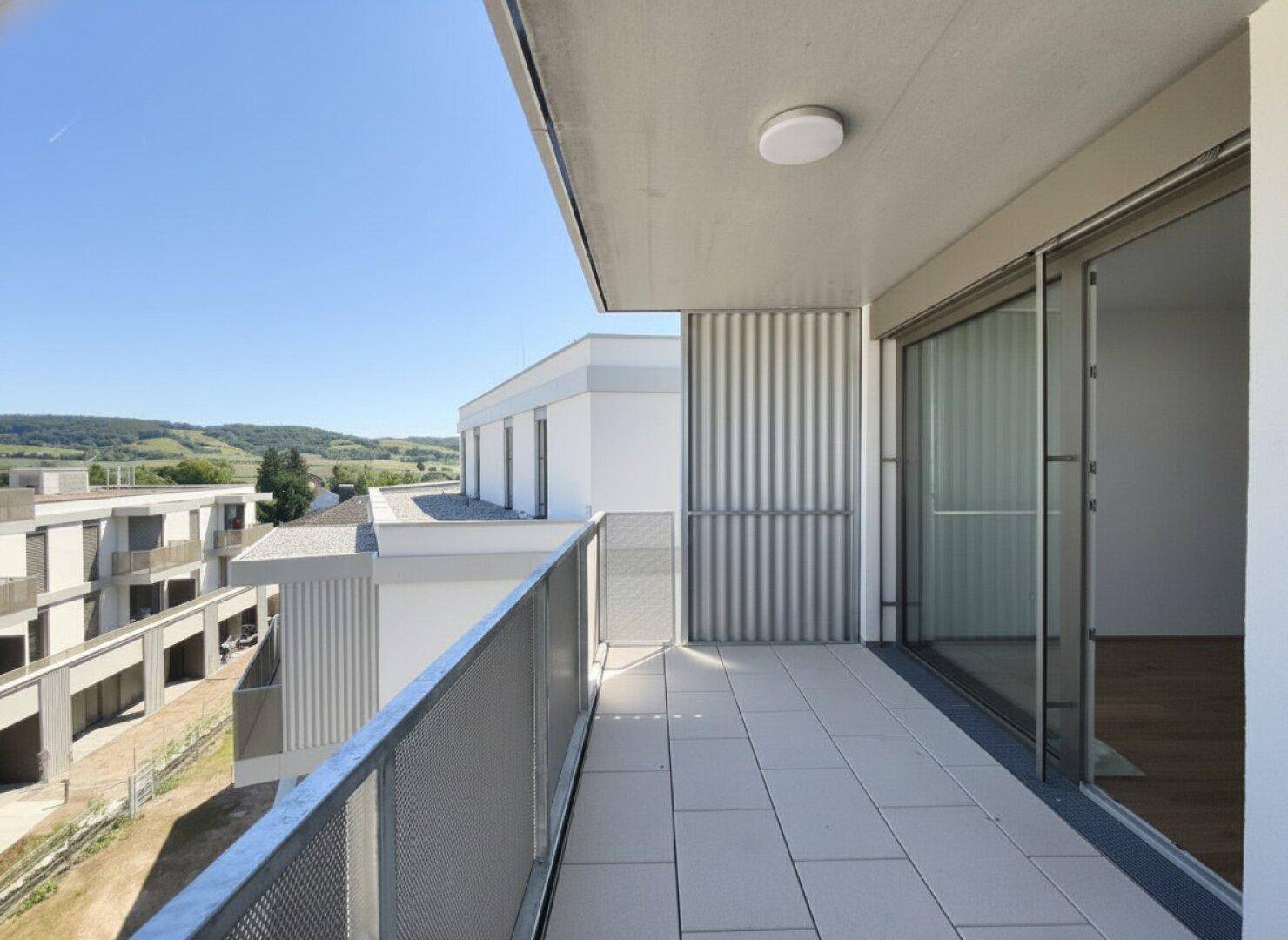 Moderner Balkon mit Fliesenboden, Metallgeländer und weitem Blick auf die Landschaft.