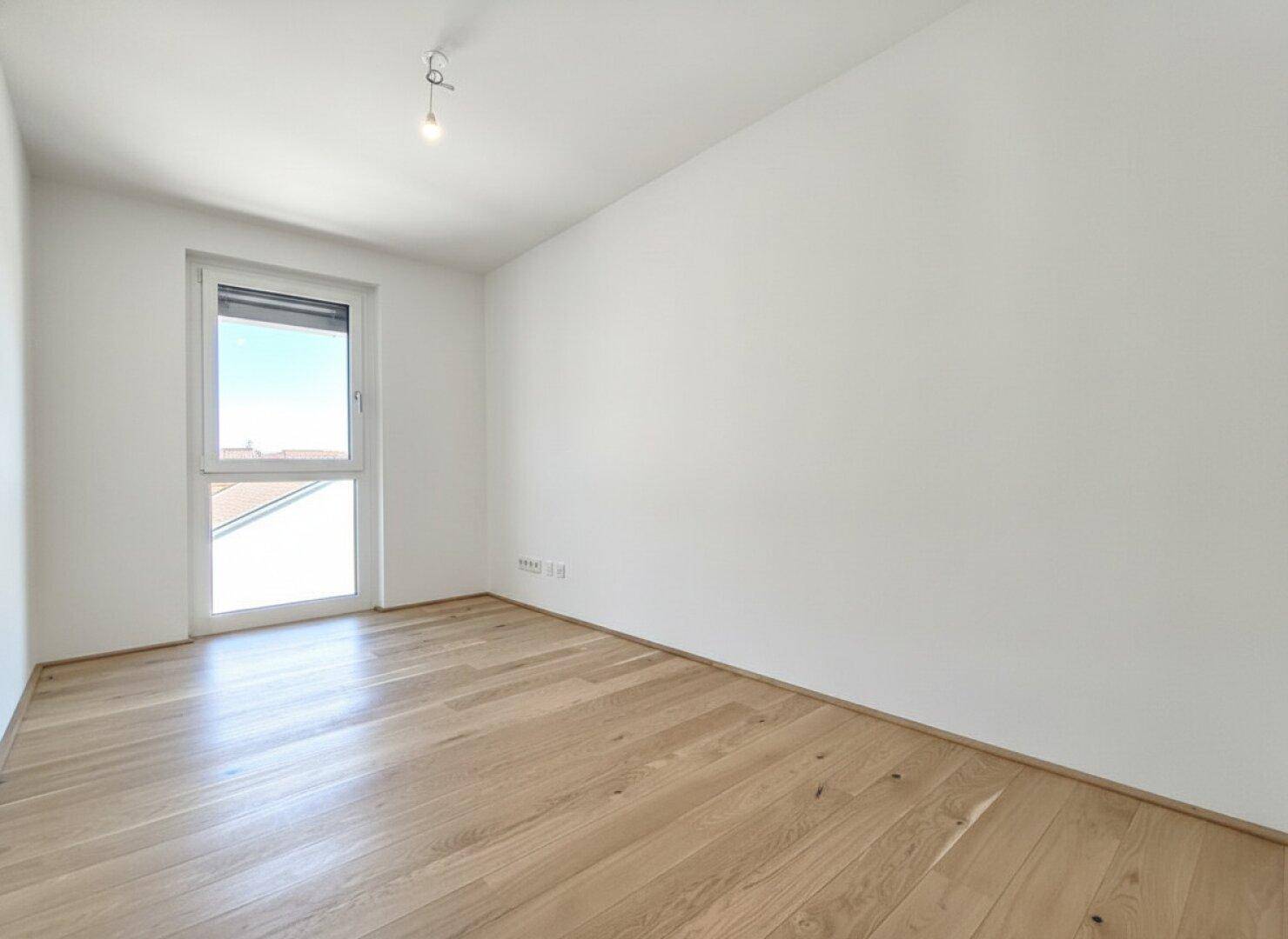 Gemütliches Schlafzimmer mit Eichenparkett und einem Fenster, das viel Tageslicht hereinlässt.