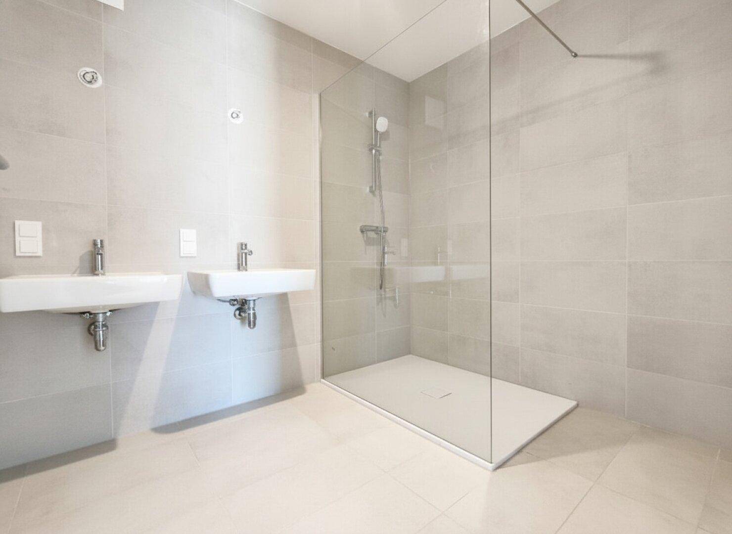 Modernes Badezimmer mit grauen Fliesen, Doppelwaschbecken und einer geräumigen begehbaren Dusche.