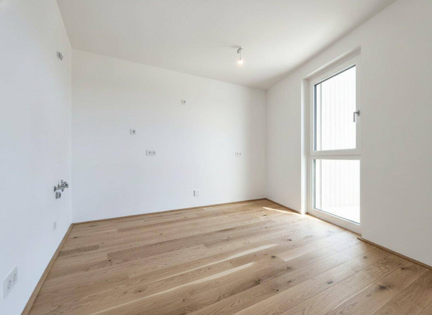 Helles Schlafzimmer mit Eichenparkett und einem großen Fenster, bereit zur individuellen Gestaltung.