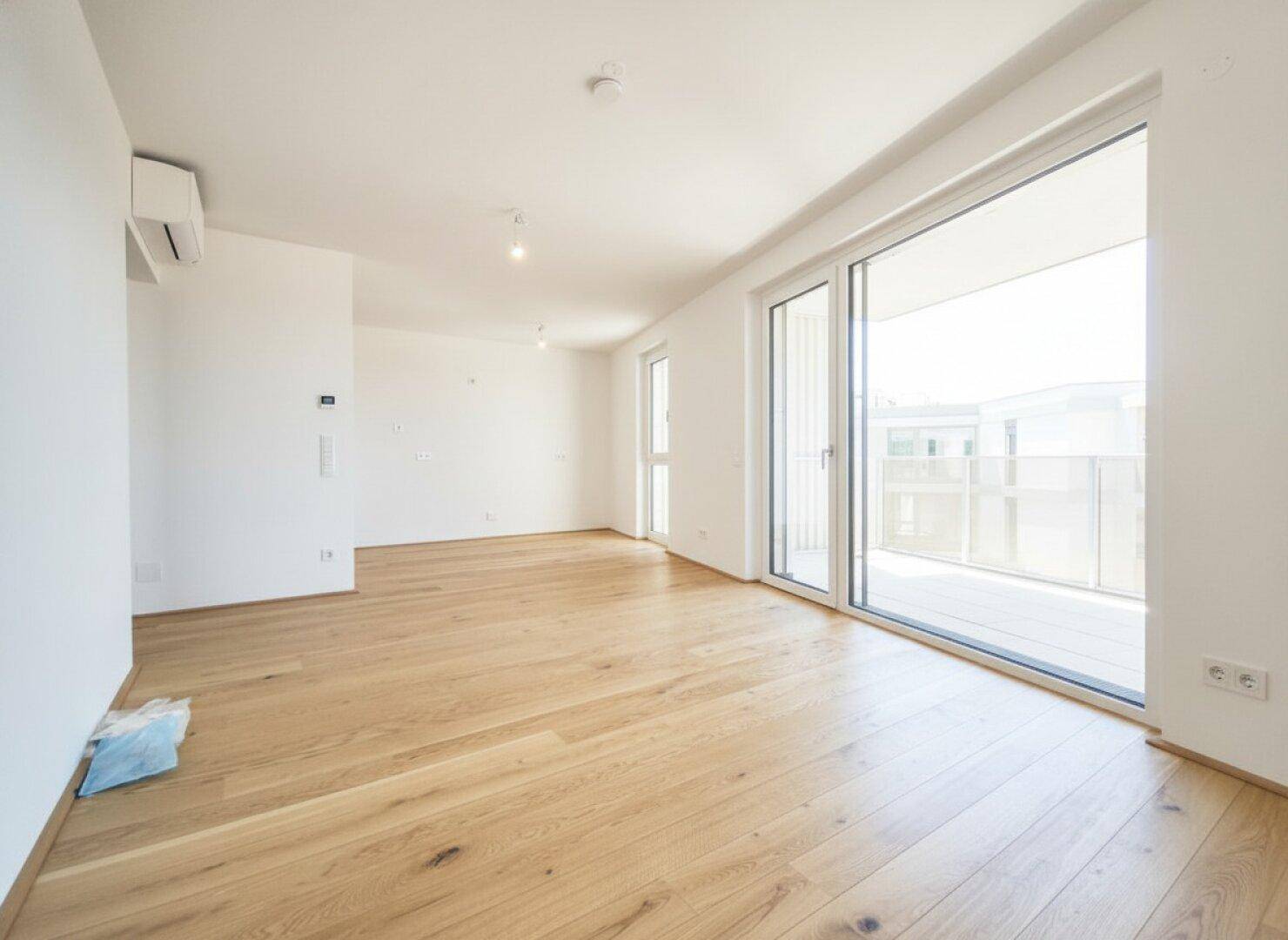 Helles, leeres Zimmer mit Eichenparkett, großen Schiebetüren zum Balkon und Klimaanlage.