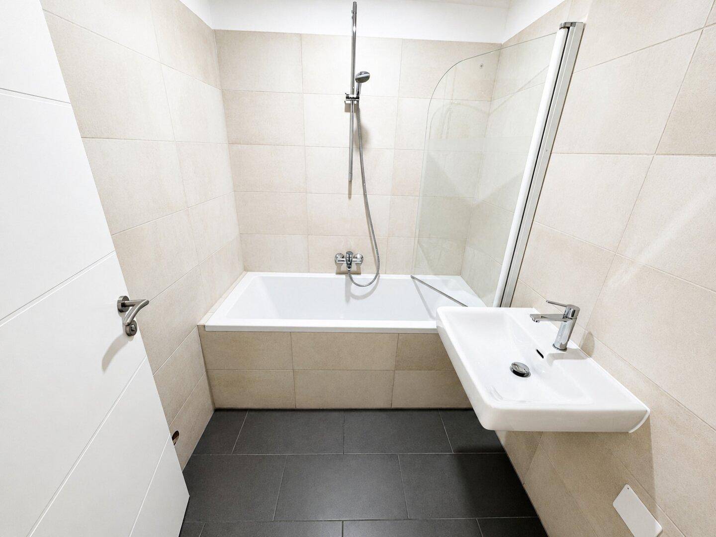 Modernes Badezimmer mit Badewanne, Einzelwaschbecken und beigen Fliesen, sehr gepflegt.