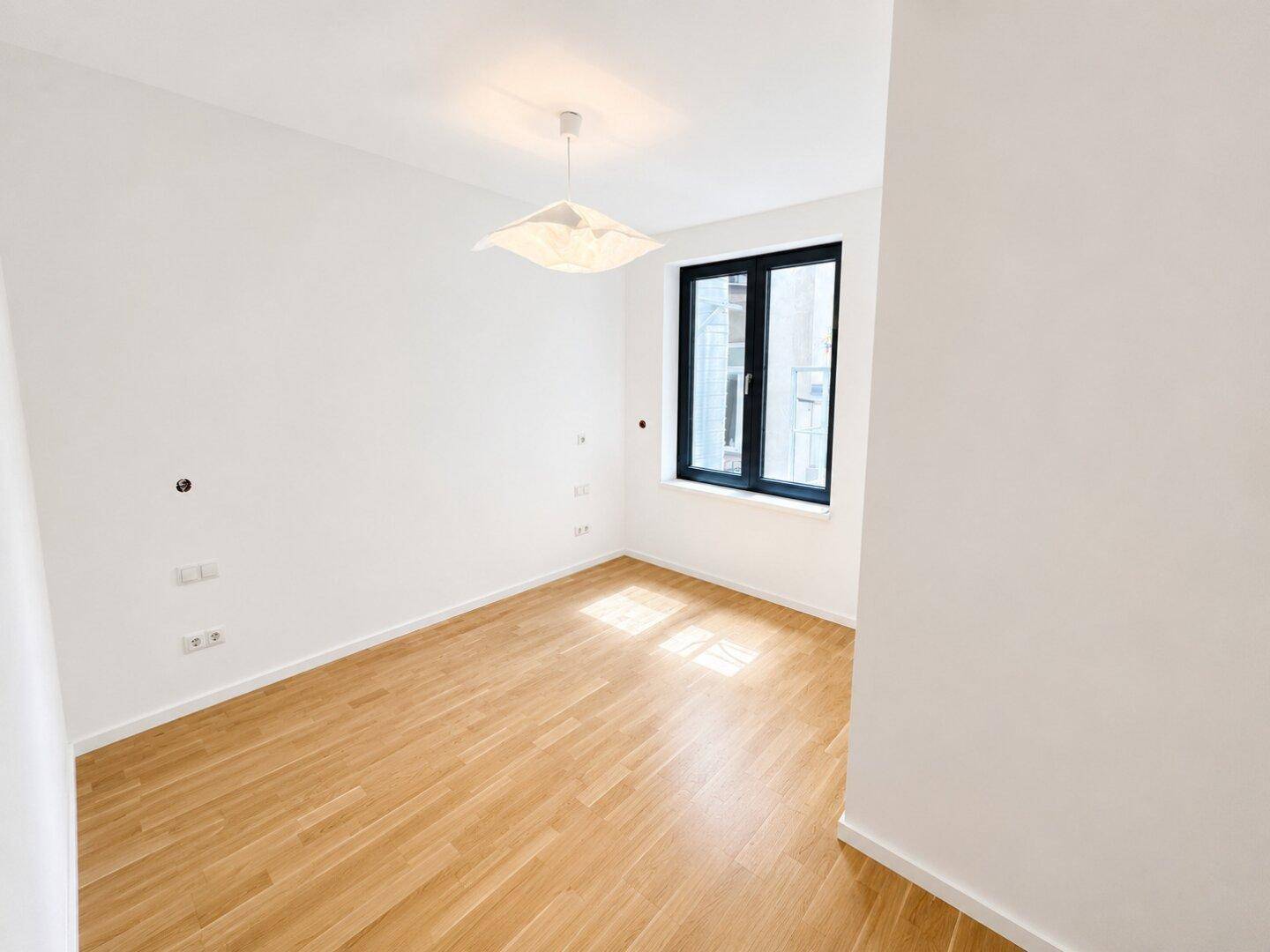 Helles Zimmer mit Holzboden und einem Fenster, das den Raum mit natürlichem Licht erfüllt.