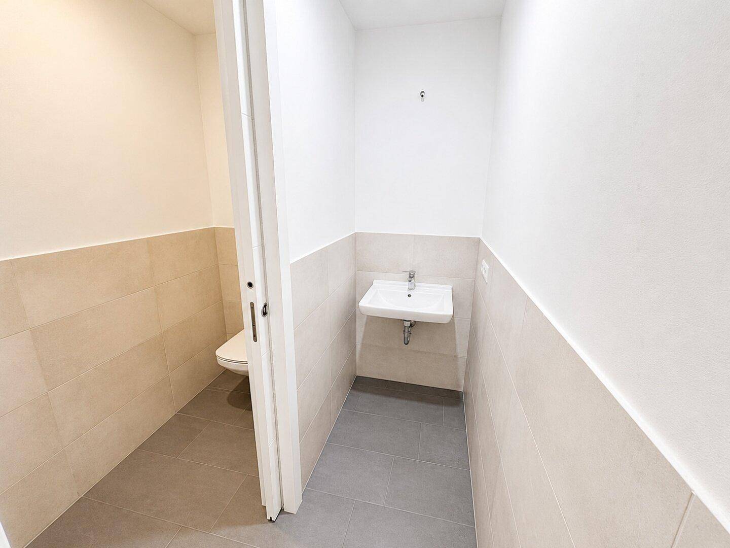 Separates Gäste-WC mit Waschbecken und Toilette, in modernen Beige- und Grautönen gehalten.