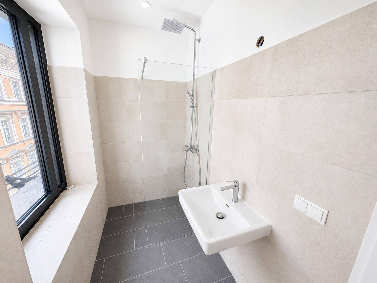 Modernes Badezimmer mit beigen Fliesen, Einzelwaschbecken und Duschbereich, gut beleuchtet.