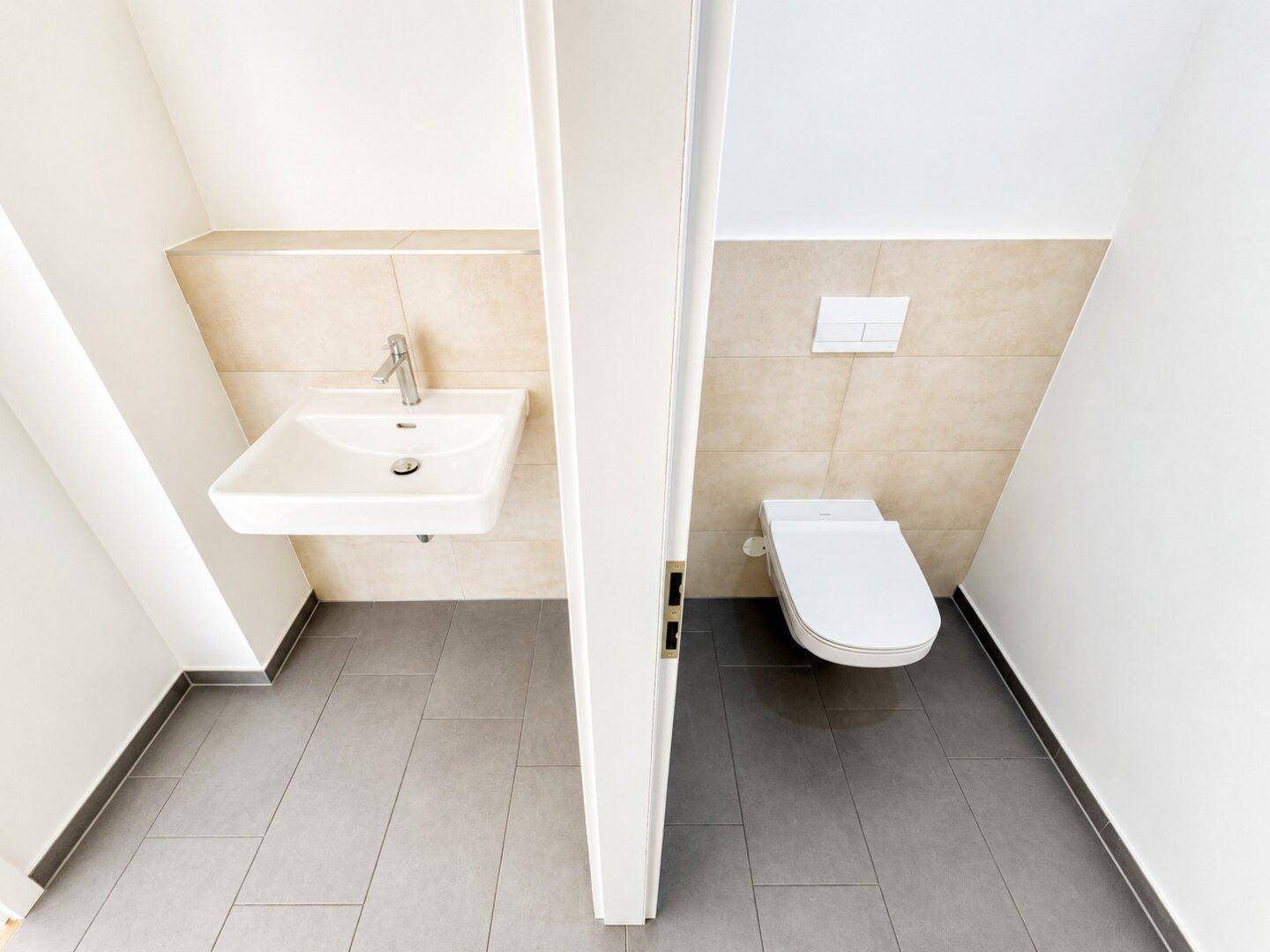 Modernes Gäste-WC mit Wand-WC und Waschbecken unter einer Dachschräge, sehr funktional.