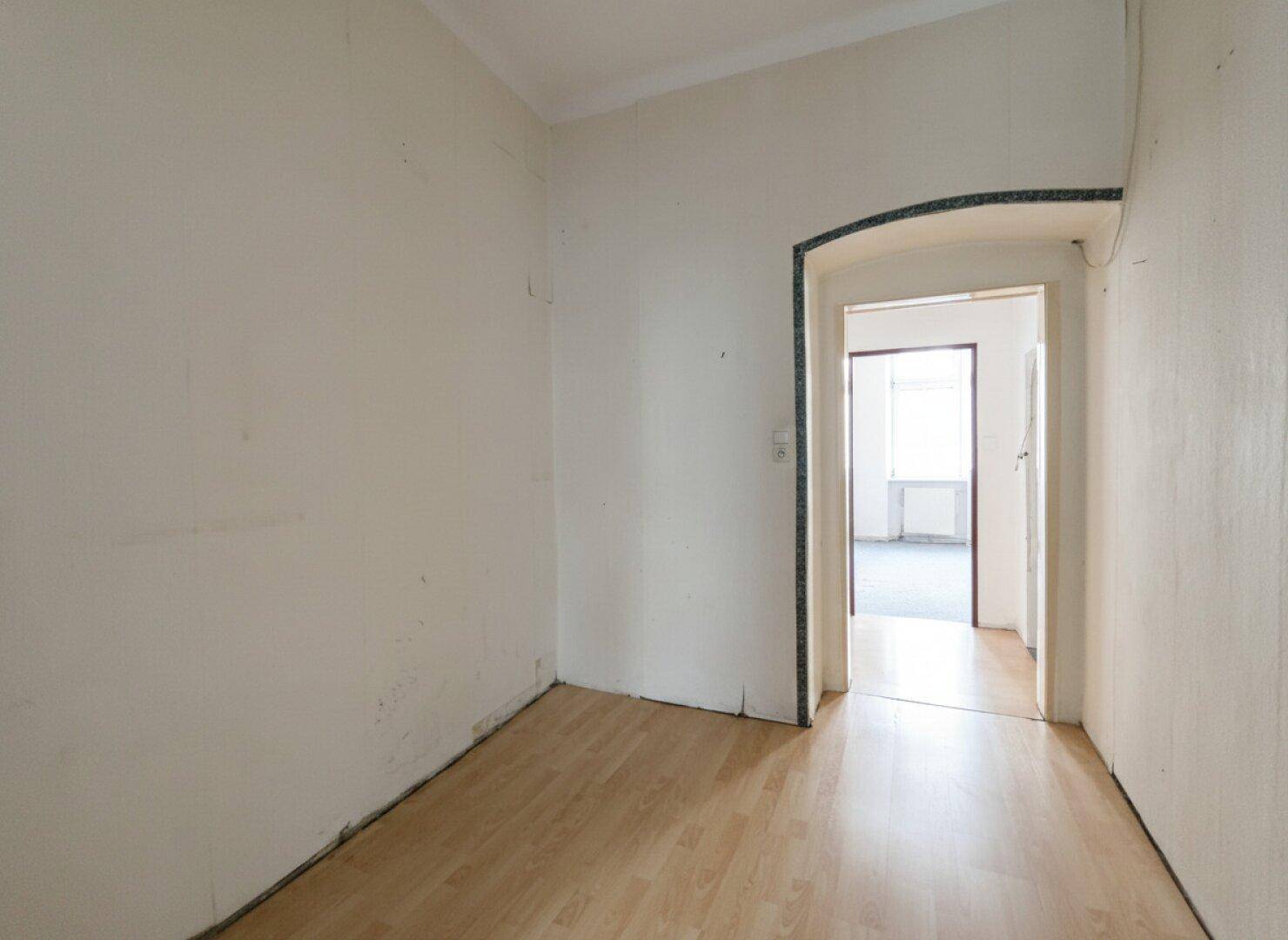 Heller Flur mit Laminatboden und einem Bogen, der in einen weiteren Raum führt.