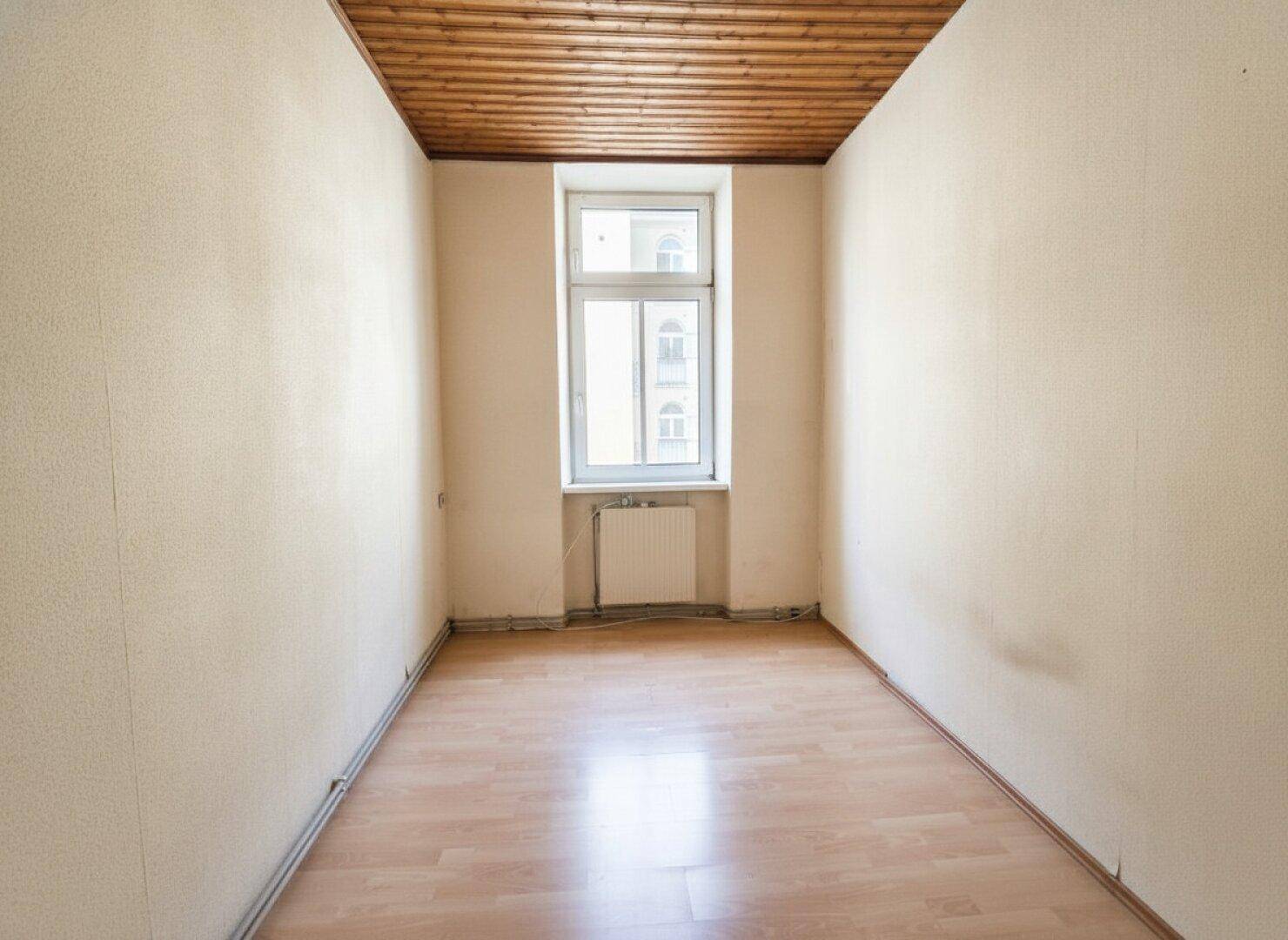 Schmaler Raum mit Laminatboden, einem Fenster und Holzpaneeldecke.