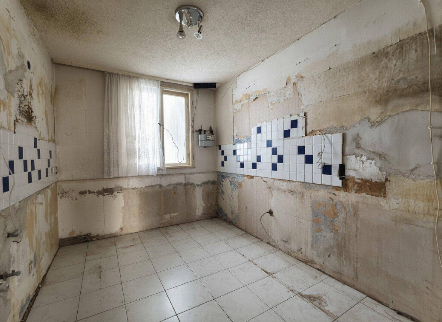 Küche in Renovierungszustand mit Fliesenboden, Fenster und teilweise gefliesten Wänden.