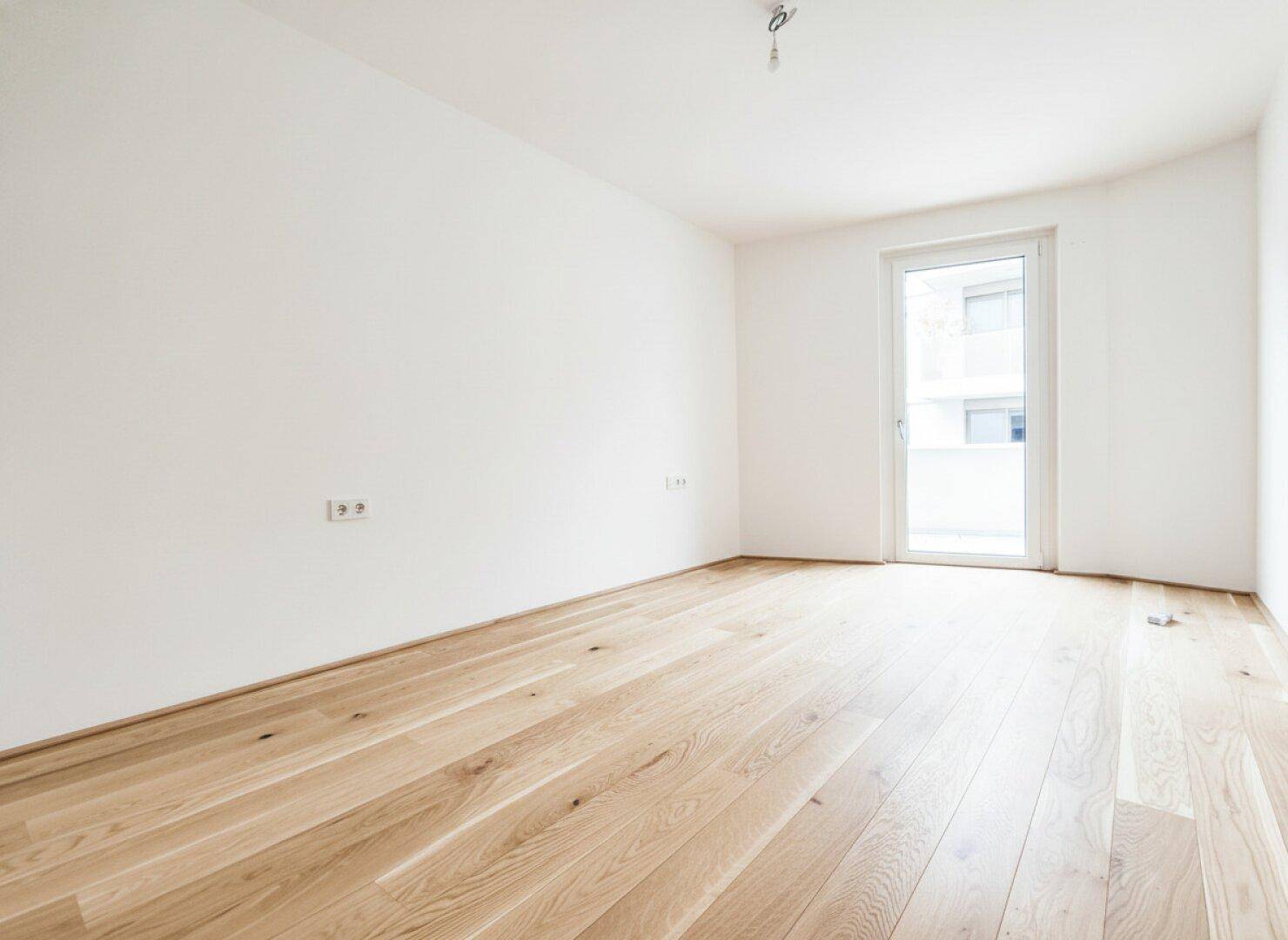 Helles Schlafzimmer mit Eichenparkett und Zugang zu einem kleinen Balkon oder einer Terrasse.