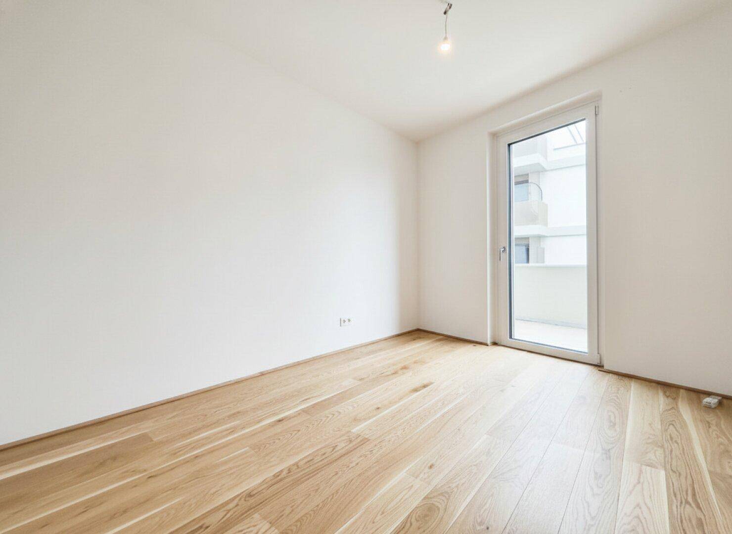 Helles Schlafzimmer mit Eichenparkett und Zugang zu einem Außenbereich, ideal für Ruhe und Erholung.