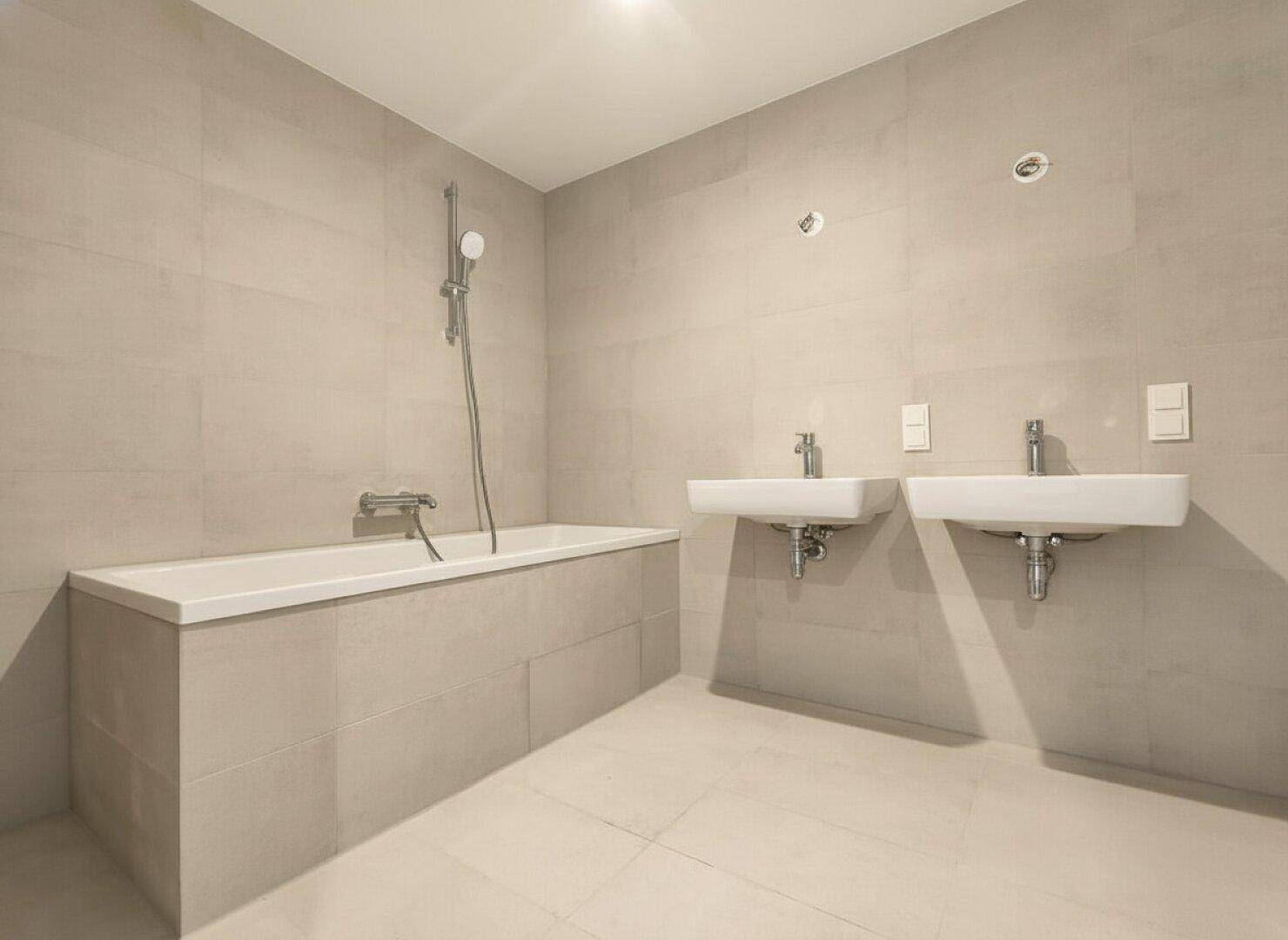 Modernes Badezimmer mit hellgrauen Fliesen, einer Badewanne und zwei stilvollen Waschbecken.