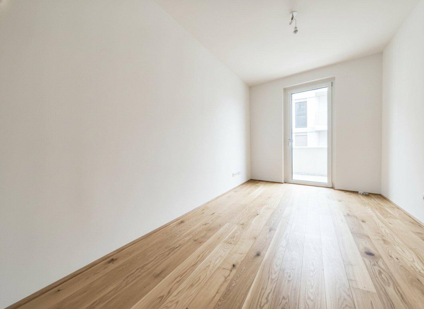 Lichtdurchflutetes Schlafzimmer mit hellem Holzfußboden und direktem Zugang zu einem Balkon oder einer Loggia.