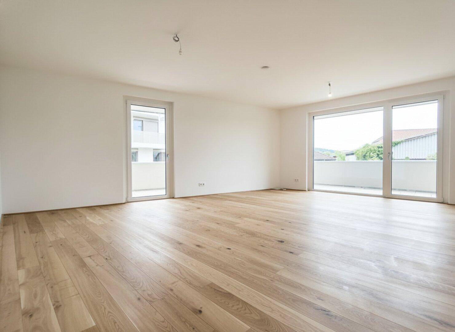 Geräumiges, helles Zimmer mit Eichenparkett und zwei Zugängen zu einem Außenbereich, ideal für Wohnen.