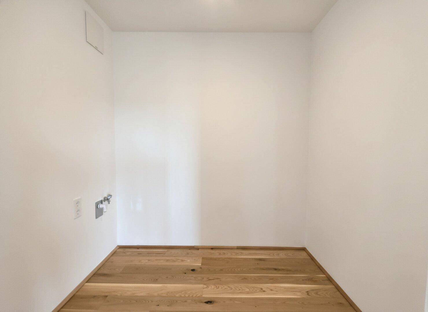 Kleiner Hauswirtschaftsraum mit Holzparkett und Anschlüssen für Waschmaschine und Trockner.
