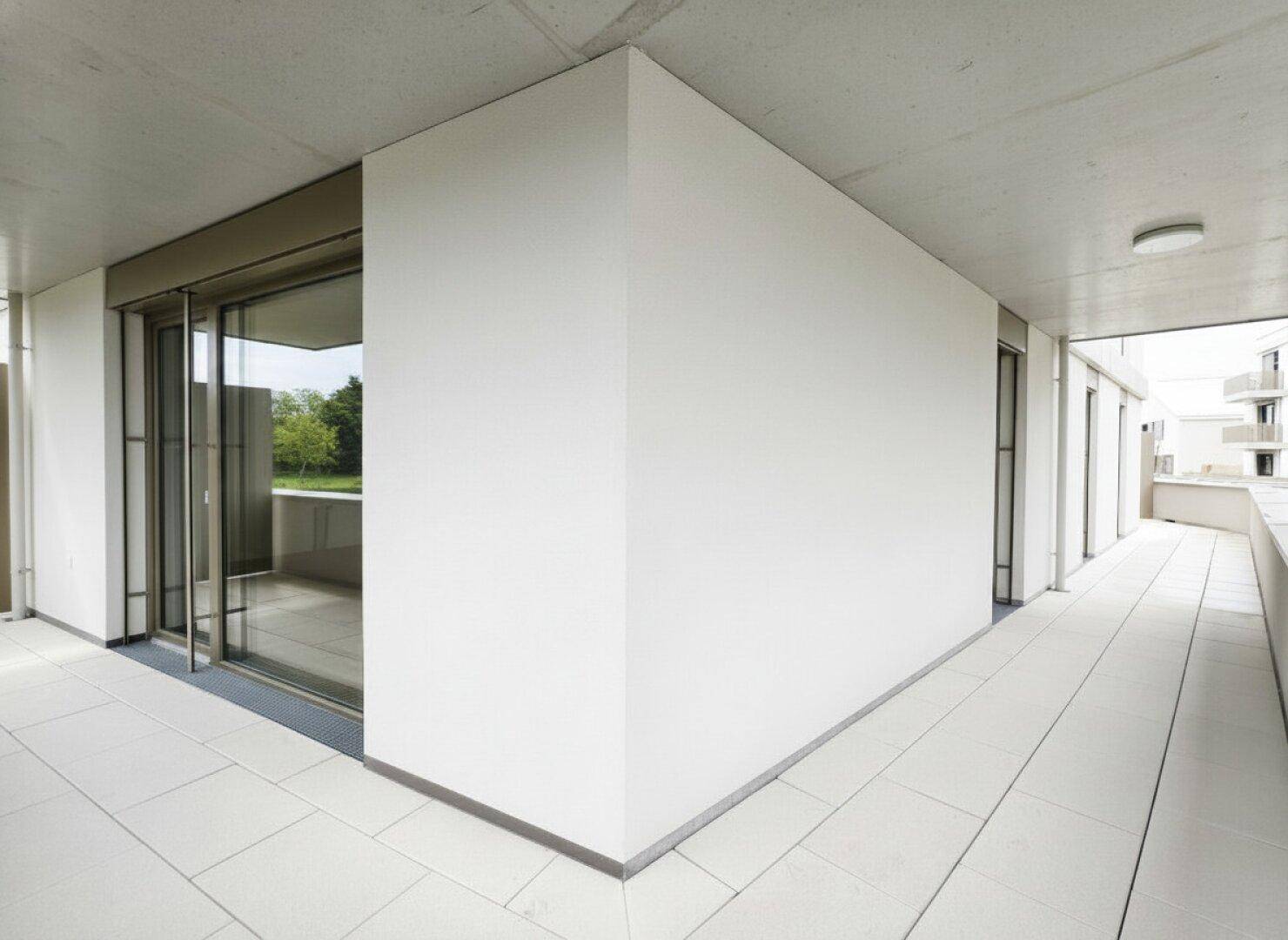Eckbereich eines modernen Balkons mit Fliesenboden und großen Glasfronten, die viel Licht hereinlassen.