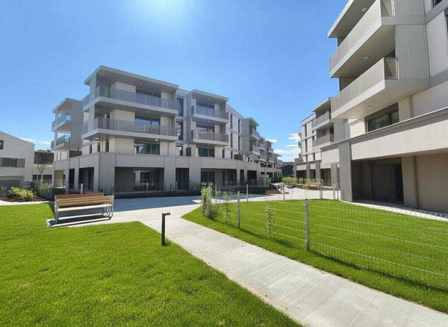 Neue Wohnanlage mit modernen Gebäuden, grünen Rasenflächen und Wegen an einem sonnigen Tag.