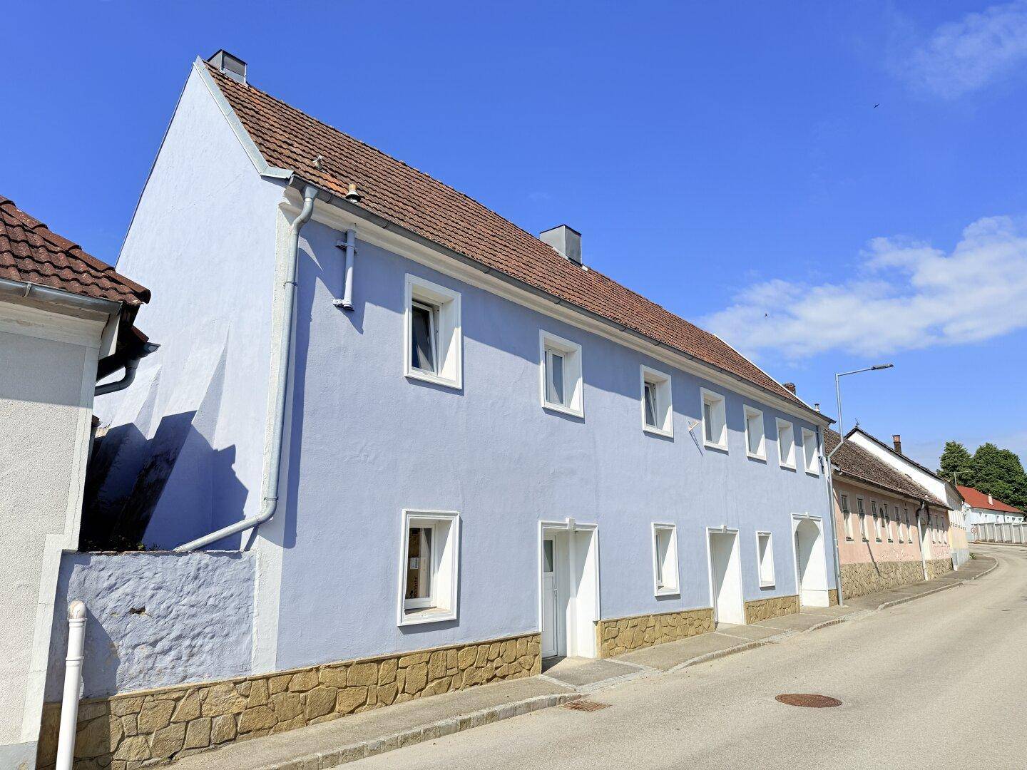 Seitenansicht des hellblauen Gebäudes mit braunem Ziegeldach und weiß gerahmten Fenstern.