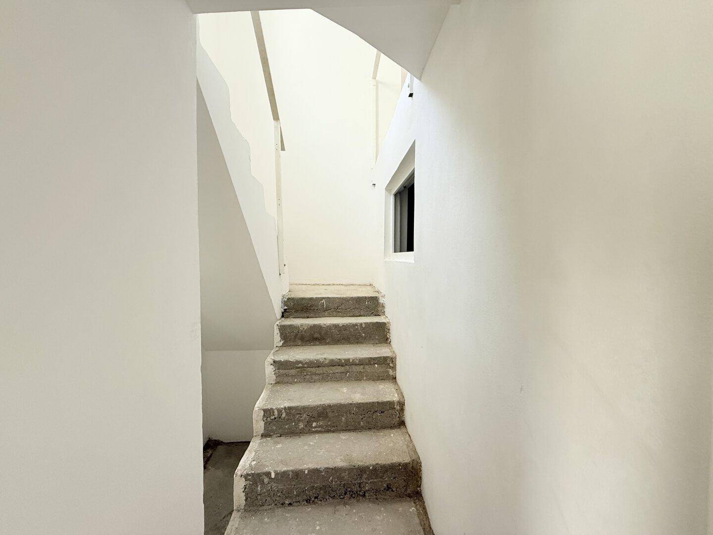Unfertiges Treppenhaus mit Betontreppe und weißen Wänden, bereit für den weiteren Ausbau.
