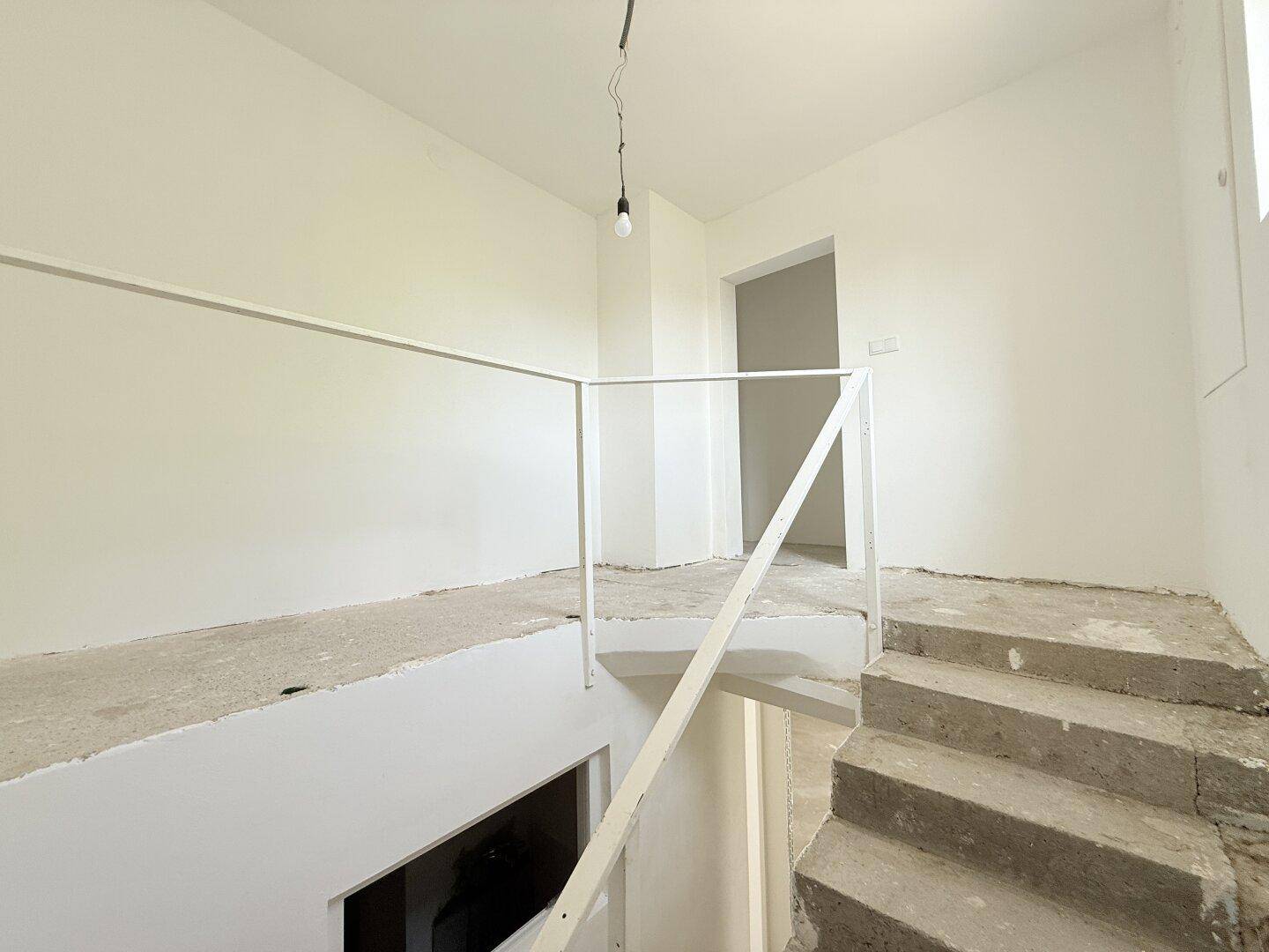Treppenabsatz mit unfertiger Betontreppe und weißem Geländer, führt zu weiteren Räumen.