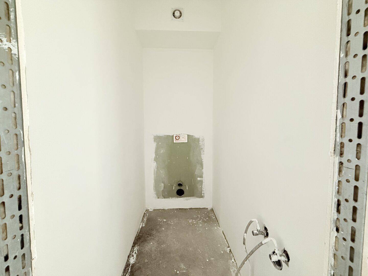 Kleiner Raum mit vorbereiteten Anschlüssen für ein WC oder Waschbecken, noch unfertig.