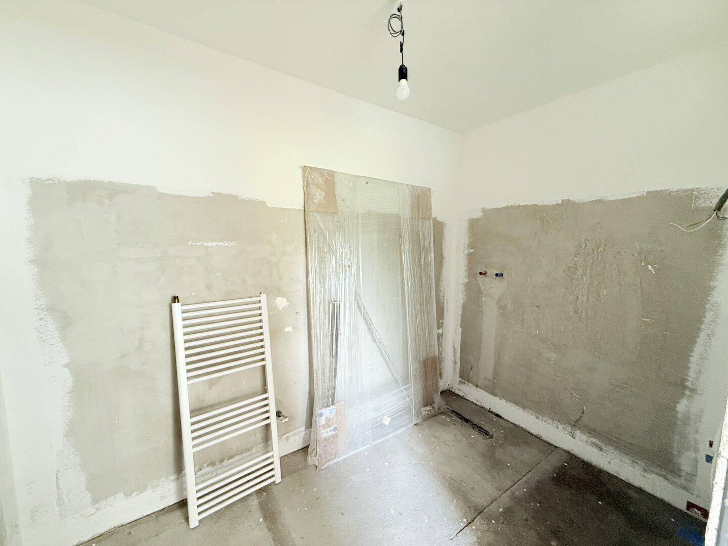 Unfertiges Badezimmer mit Heizkörper und vorbereiteten Wänden, wartet auf die Endmontage.