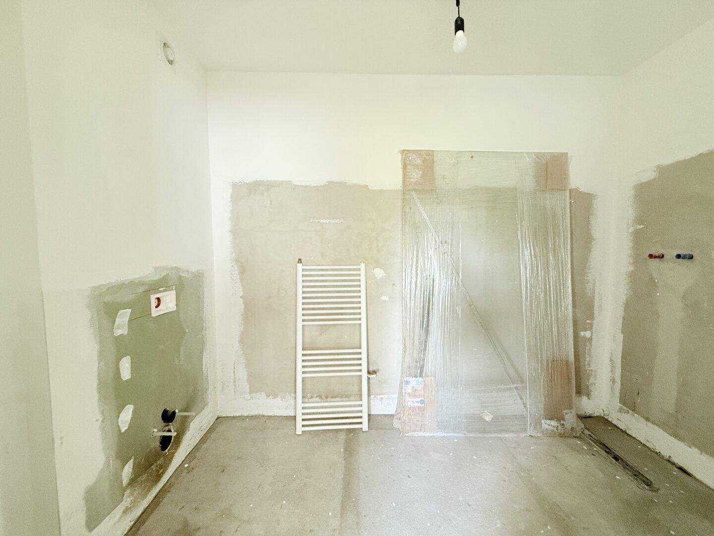 Unfertiges Badezimmer mit Heizkörper und vorbereiteten Wänden, wartet auf die Endmontage.