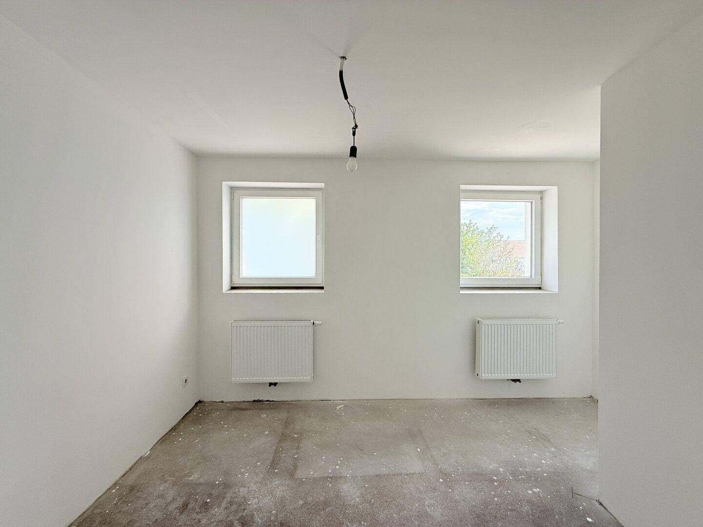 Heller, unfertiger Raum mit zwei Fenstern und Heizkörpern, ideal als Schlafzimmer.