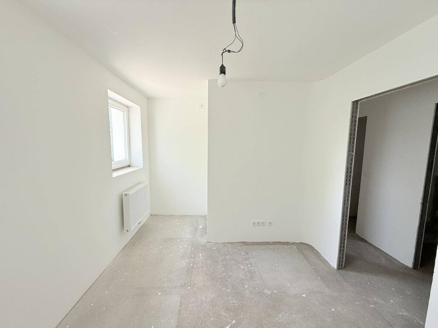 Heller, unfertiger Raum mit einem Fenster und Heizkörper, ideal als Schlaf- oder Arbeitszimmer.