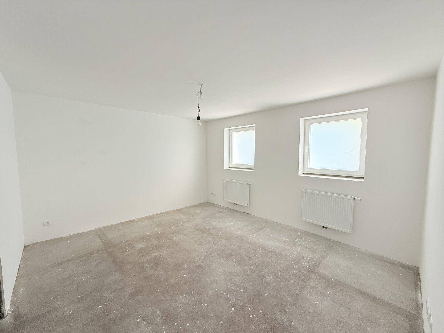 Heller, unfertiger Raum mit zwei Fenstern und Heizkörpern, ideal als Schlafzimmer.