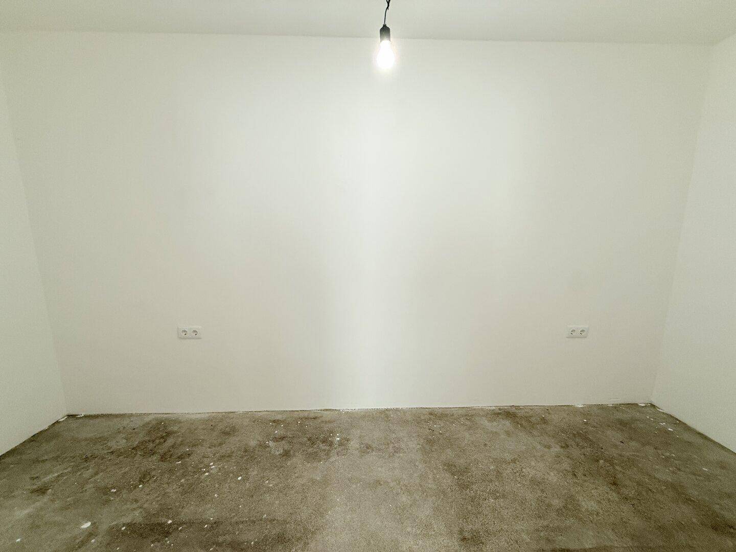 Leerer Raum mit weiß gestrichenen Wänden und einem einzelnen Lichtanschluss an der Decke.