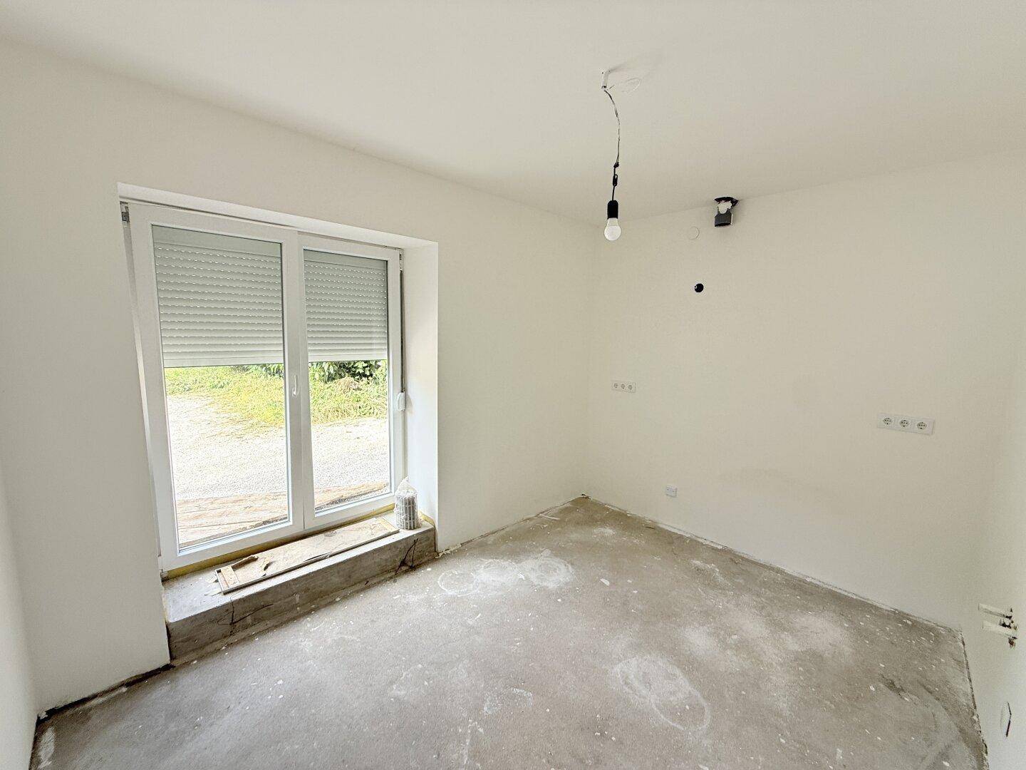 Heller, unmöblierter Raum mit großem Fenster und Rollladen, bereit für die individuelle Einrichtung.