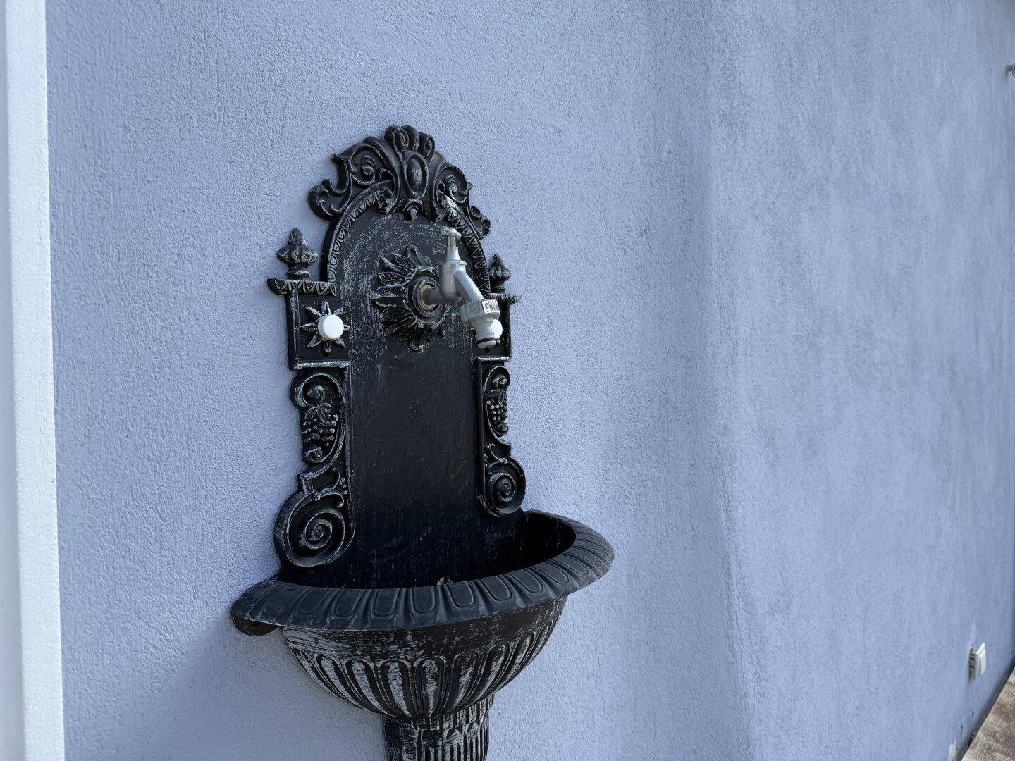 Dekorativer Wasserhahn im Vintage-Stil an einer hellblauen Außenwand des Hauses.