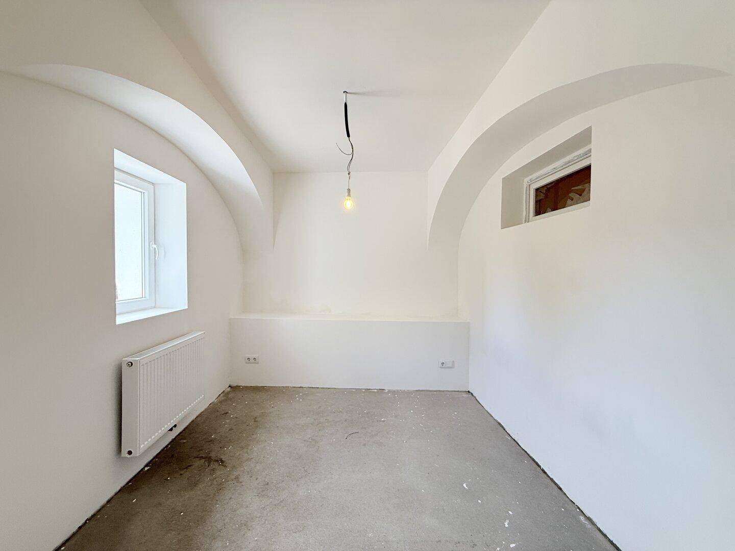 Heller Raum mit Gewölbedecken, Betonboden und einem Fenster, bereit für die Gestaltung.